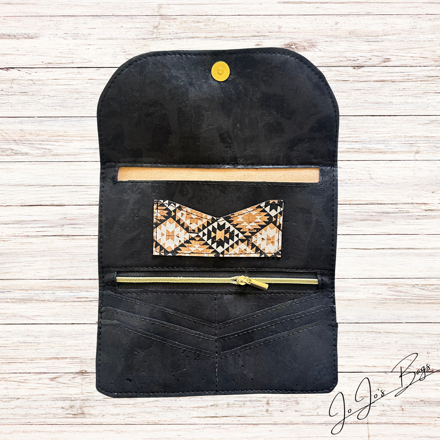 A cork wallet or organizer pouch with a gold snap button, shown open on a light wood background. Inside, there is a horizontal card slot, a patterned zip pocket with a geometric brown, beige, and black design, and a gold zipper pull.