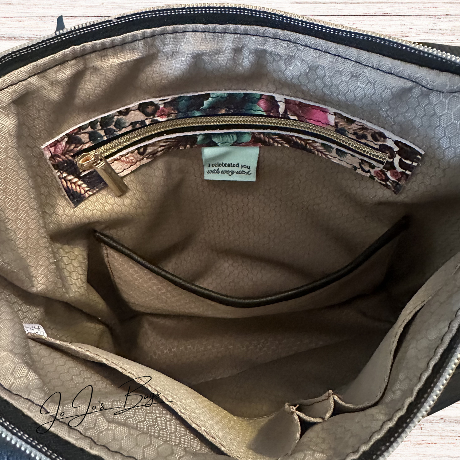 Close-up of the interior of a beige textured interior bag, showing a zippered pocket with a floral-patterned trim and a small fabric label.