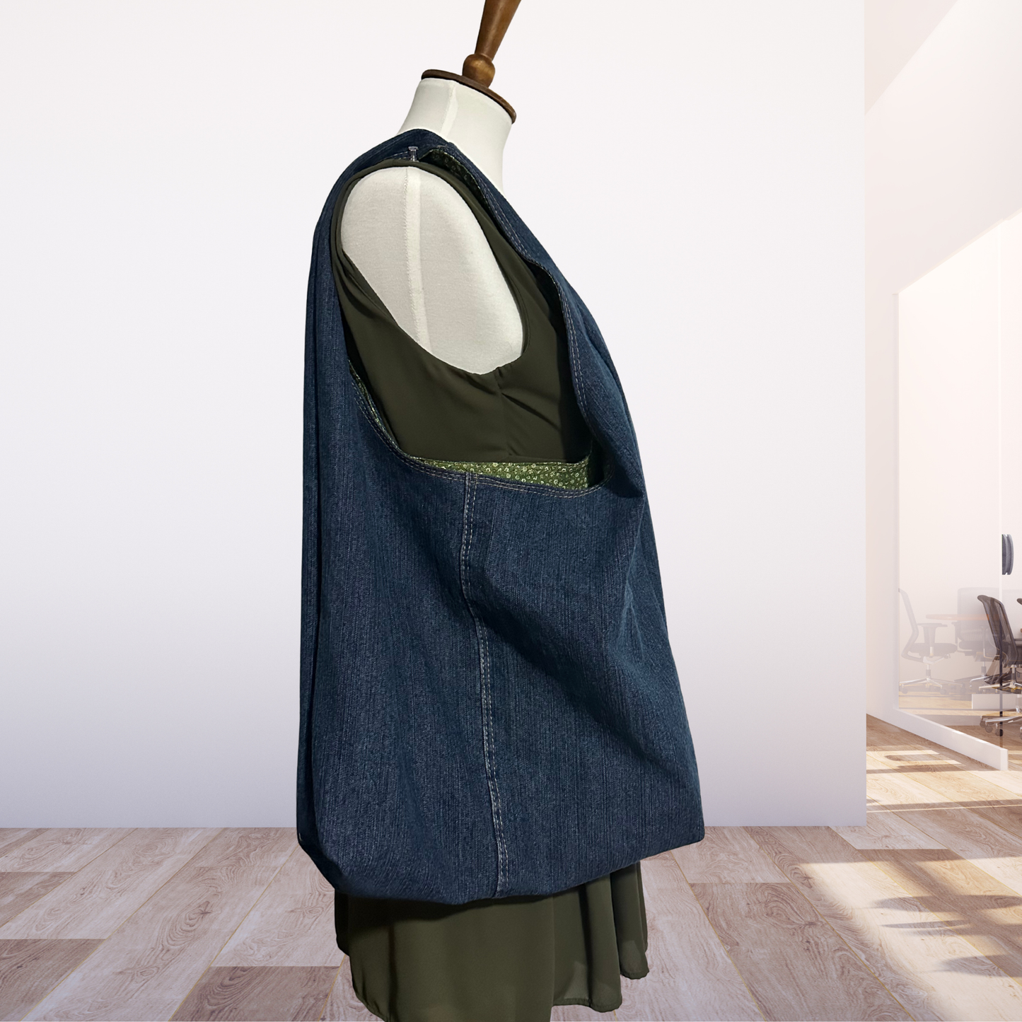 Mannequin holding a blue denim bag over green dress on a wooden floor.