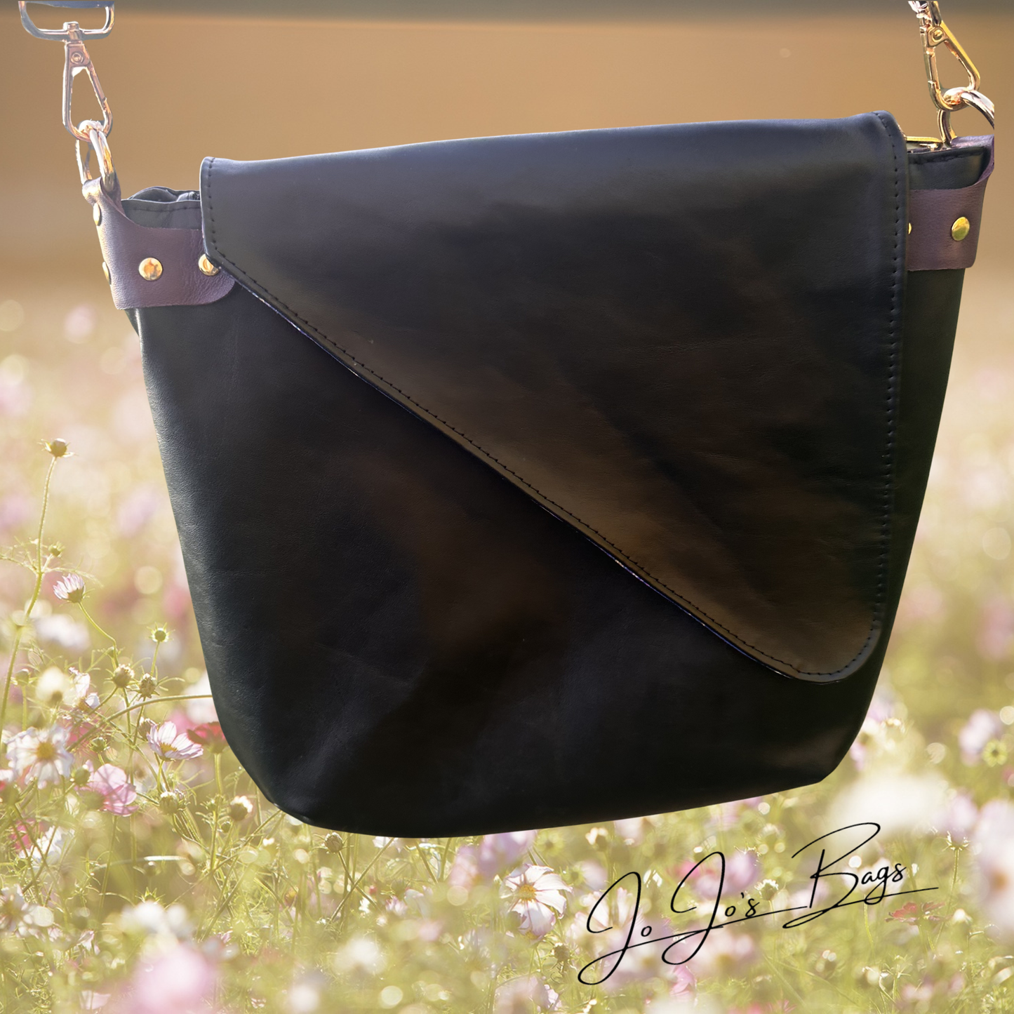 A black leather shoulder bag with a diagonal flap closure and gold-tone hardware, shown against a blurred outdoor floral background. The brand name 'Jo Jos Bags' is visible as a watermark in the lower right corner.