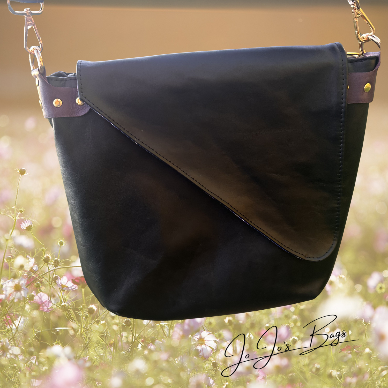 A black leather shoulder bag with a diagonal flap closure and gold-tone hardware, shown against a blurred outdoor floral background. The brand name 'Jo Jos Bags' is visible as a watermark in the lower right corner.