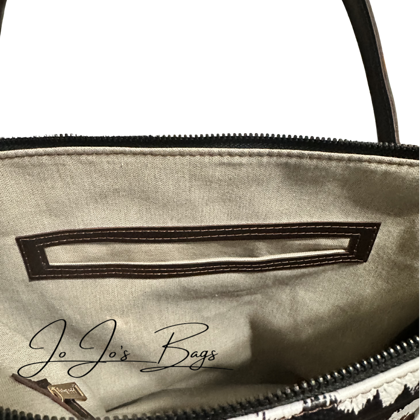 Close-up of the interior of a handbag showing a beige fabric lining, a dark brown stitched slot pocket, zipper trim, and part of a black-and-white patterned exterior. A script logo reading 'Jo Jo's Bags' is visible on the lining.