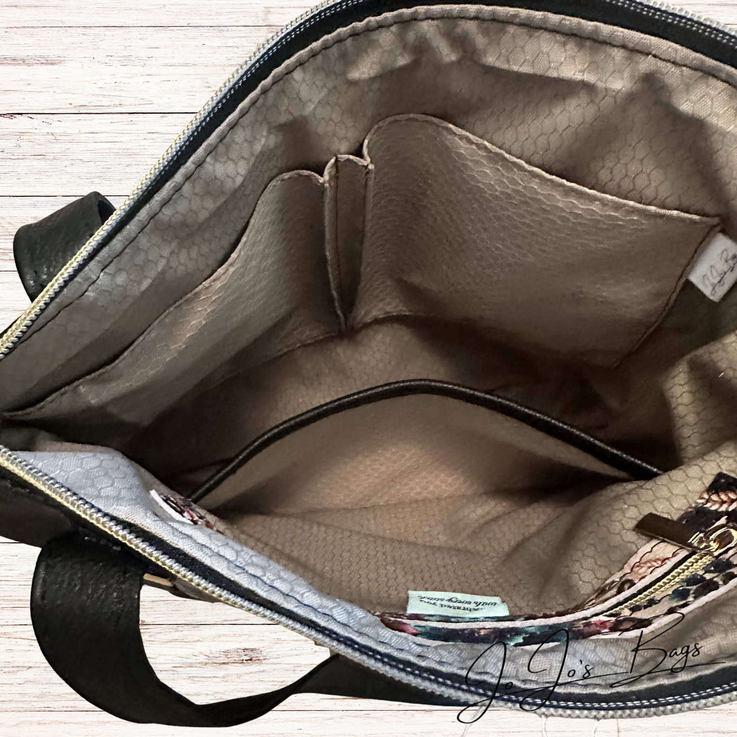 Open view of a handbag interior showing a structured beige  honeycomb-patterned lining with multiple compartments, black trim, and a small patterned zippered pocket near the bottom right.