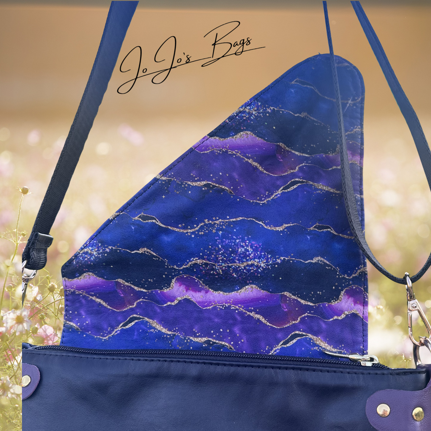 A close-up of a handbag showing the interior lining, which has a blue and purple marbled pattern with gold glitter accents. The exterior of the bag is black with gold hardware.